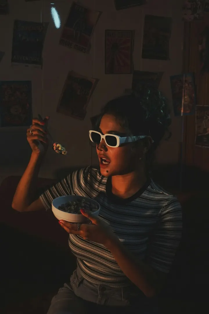 Una persona con gafas blancas come cereal de un bowl en una habitación llena de pósteres. Fotografía de referencia.